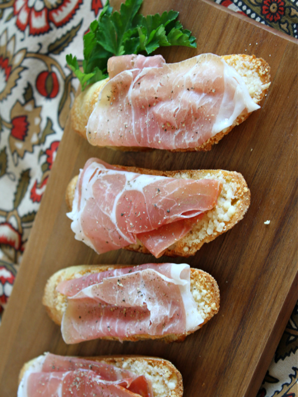 cheese crostini with prosciutto on serving board