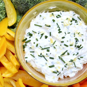 overhead shot of lemon chive cheese dip in a yellow bowl surrounded by yellow peppers, broccoli and carrots