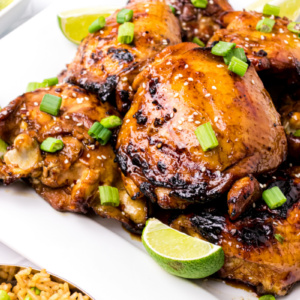 asian barbecue chicken on a white platter with chives and lime