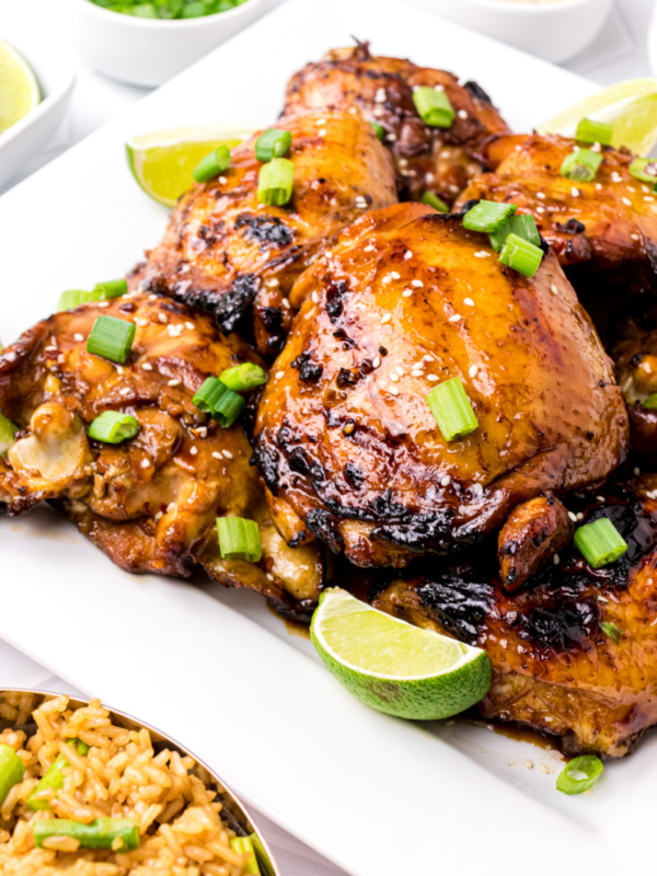 asian barbecue chicken on a white platter with chives and lime