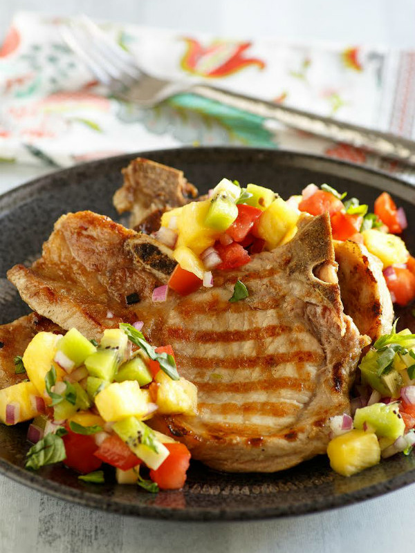 Grilled Pork Chops with tropical salsa on top set on a black dinner plate and a flowered napkin in the background