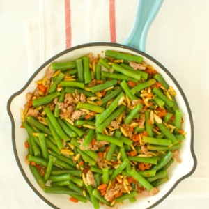 overhead shot of green beans with prosciutto in a fry pan with a blue handle, set on a yellow napkin with red stripes