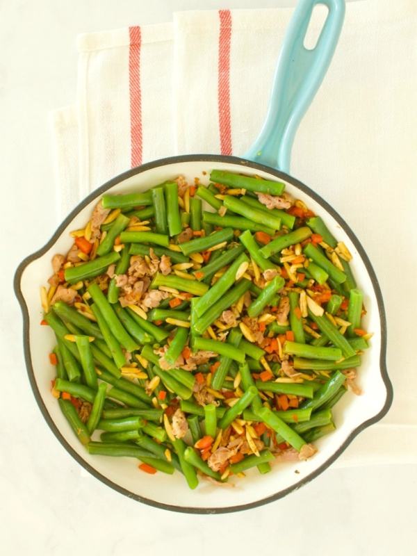 overhead shot of green beans with prosciutto in a fry pan with a blue handle, set on a yellow napkin with red stripes