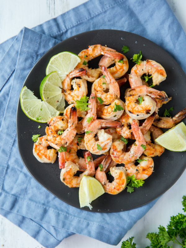 Marinated Grilled Shrimp on a black plate set on a blue napkin with lime and cilantro garnish