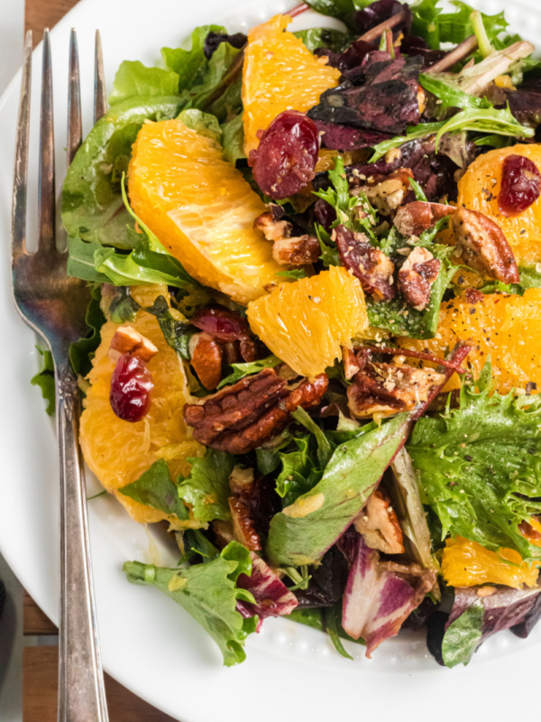 mixed green salad with oranges and dried cranberries on white plate with fork