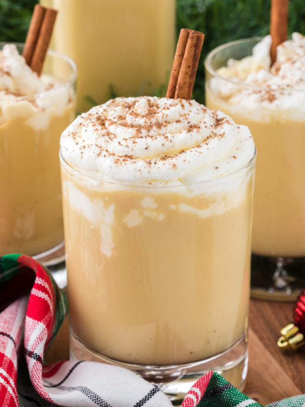 spiked eggnog in a glass mug with whipped cream and cinnamon stick