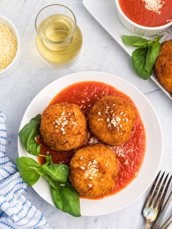 three risotto croquettes on a plate of marinara sauce