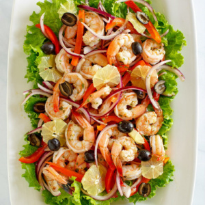 overhead shot of spicy lemon shrimp salad surrounded by green lettuce leaves on a white platter