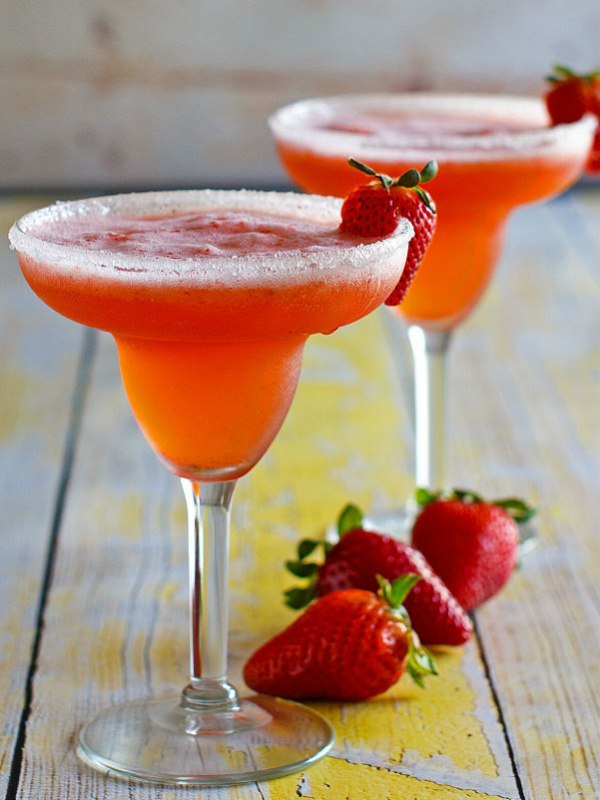 two strawberry margaritas in margarita glasses garnished with strawberries