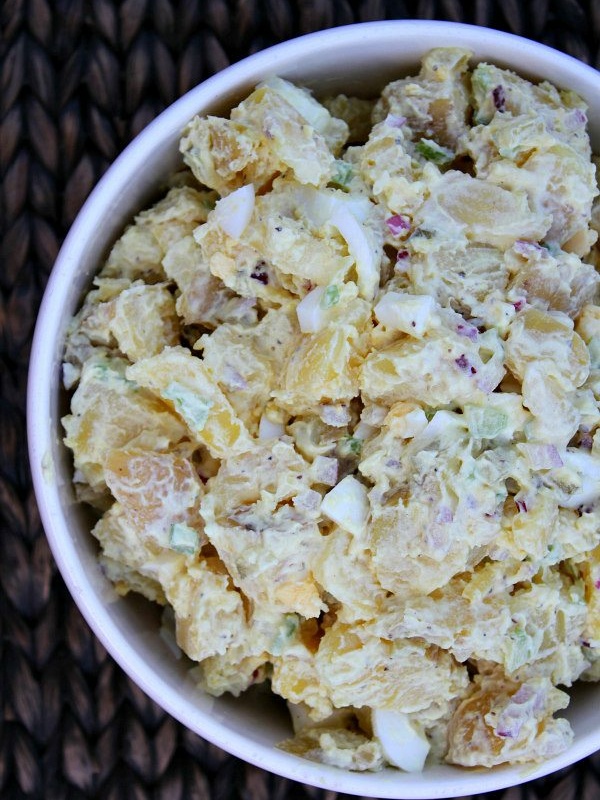 overhead shot of all american potato salad in a white bowl set on a woven placemat