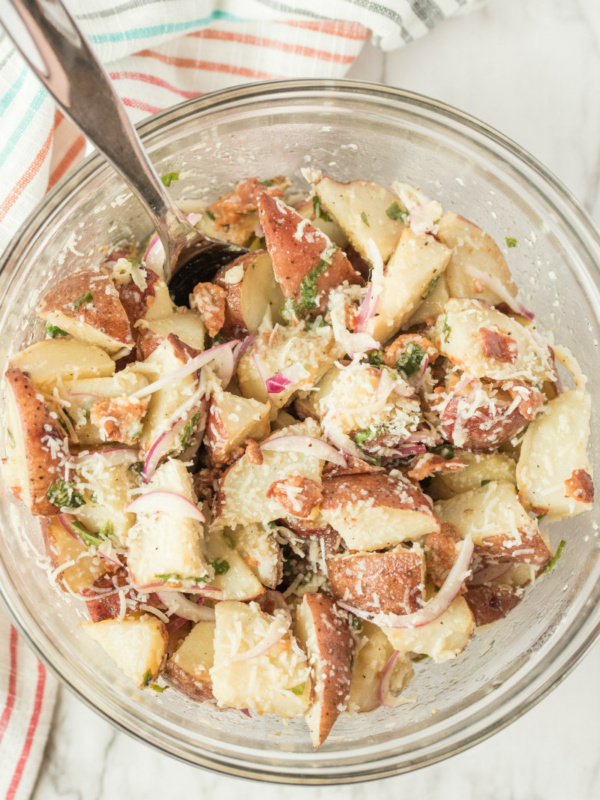 overhead shot of glass bowl with lemon basil roasted potato salad with a spoon set on a striped cloth napkin