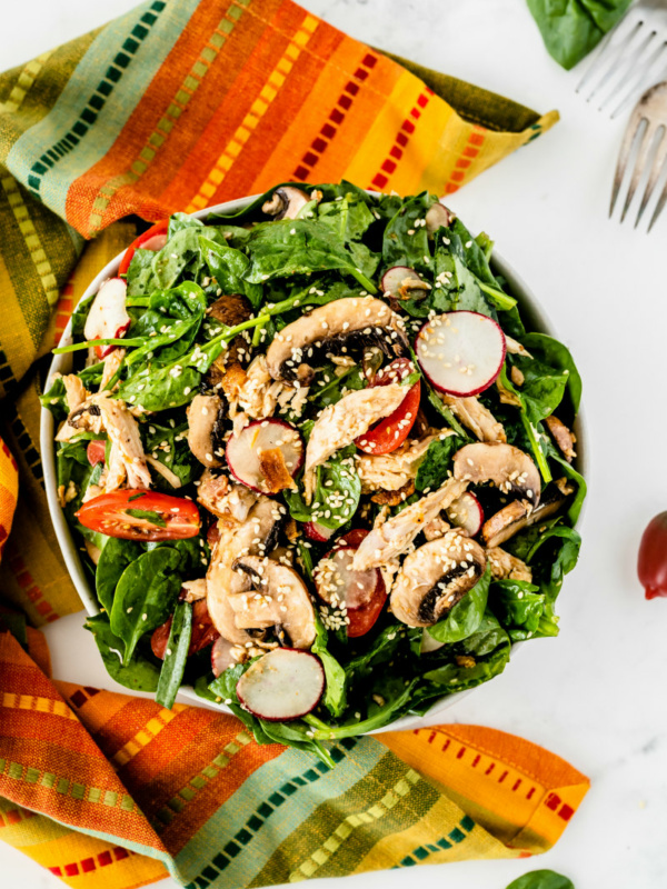 overhead shot of mandarin chicken spinach salad set on a bright striped cloth napkin