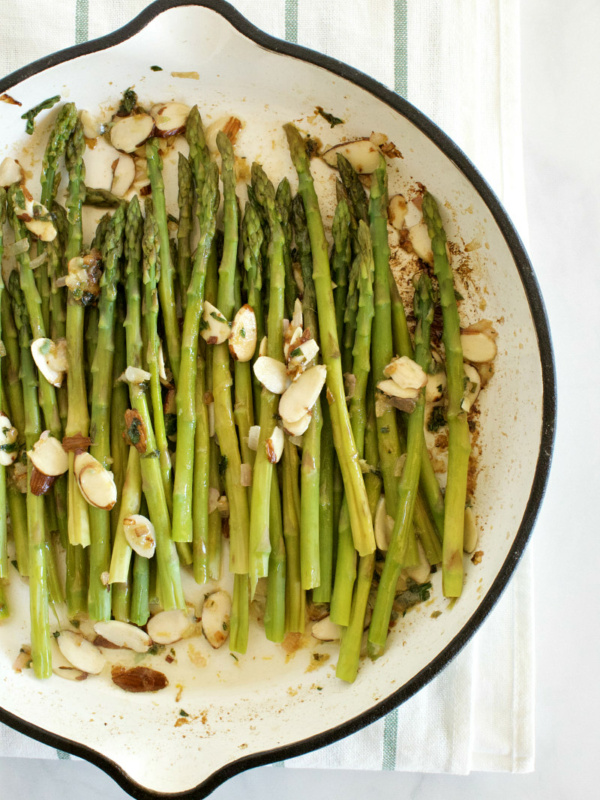 overhead shot of asparagus and almond butter in a white enamel skillet set on a white napkin with blue stripes