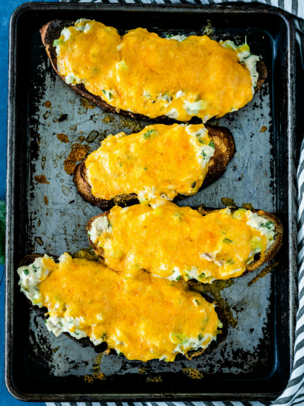 overhead shot of four tuna melts on a baking sheet set on a blue and white striped towel