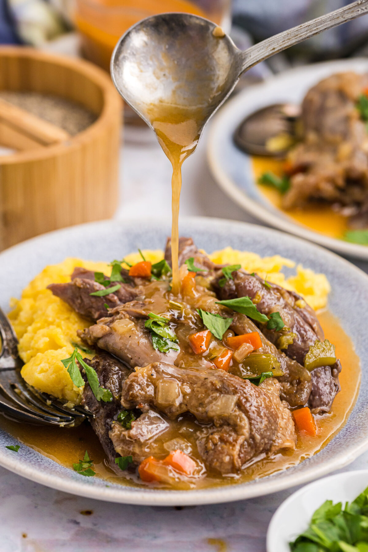 pouring gravy over plating of lamb osso buco