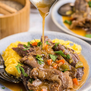 pouring gravy over plating of lamb osso buco