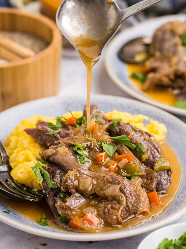 pouring gravy over plating of lamb osso buco