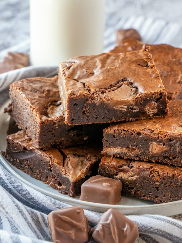 stack of milky way brownies on a plate with a glass of milk in the background- all on a striped blue and white napkin