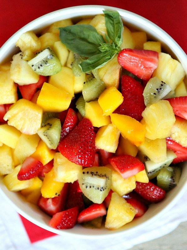 overhead shot of basil lime fruit salad in a white bowl set on a red napkin