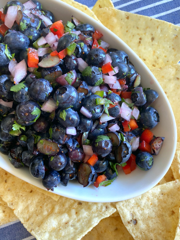 blueberry salsa in a white bowl surrounded by tortilla chips on a white/blue striped napkin