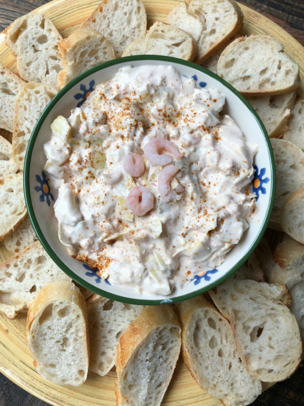 Overhead shot of a bowl of chili shrimp dip surrounded by baguette slices