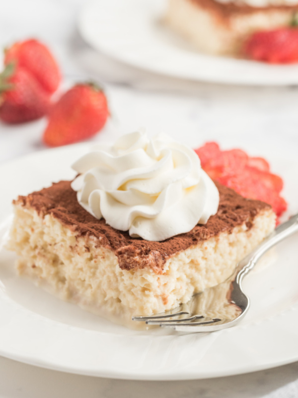 slice of tres leches cake on a white plate with whipped cream and strawberry