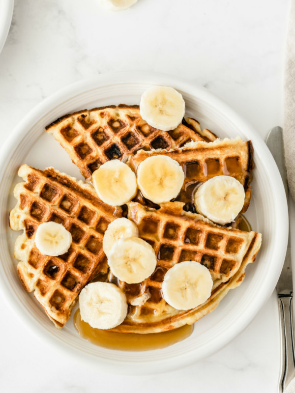 white plate with banana sour cream waffles. Sliced bananas on top