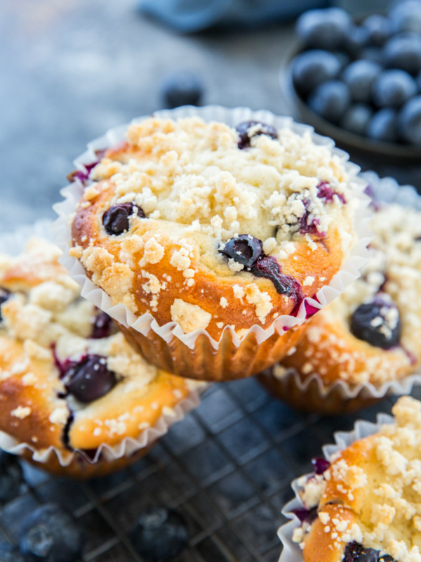 blueberry muffin sitting on top of other blueberry muffins with fresh blueberries in the background