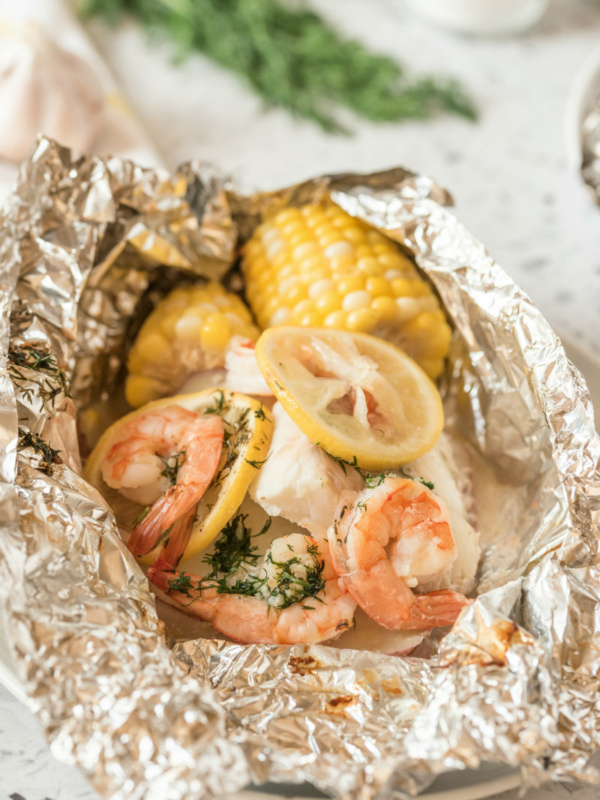 grilled new england seafood foil packets opened up to see the inside. fresh herbs in background