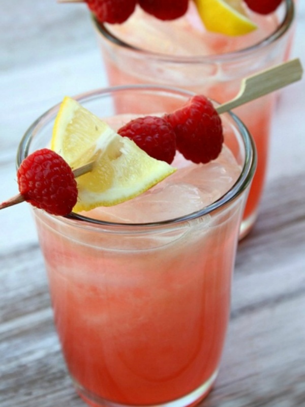 two glasses of spiked raspberry lemonade with a toothpick garnish of raspberries and lemon on top