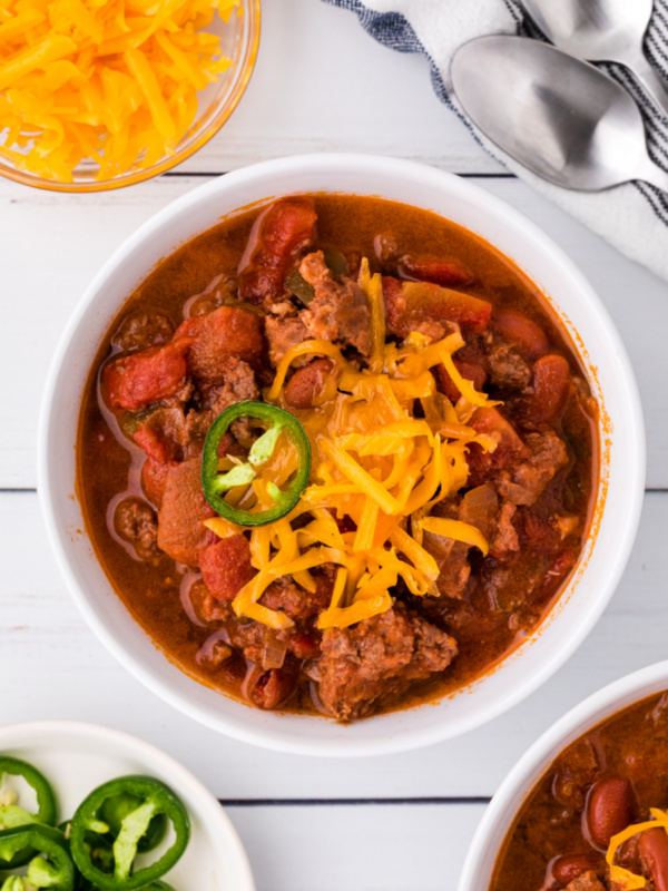 white bowl of chili topped with cheese and jalapeno