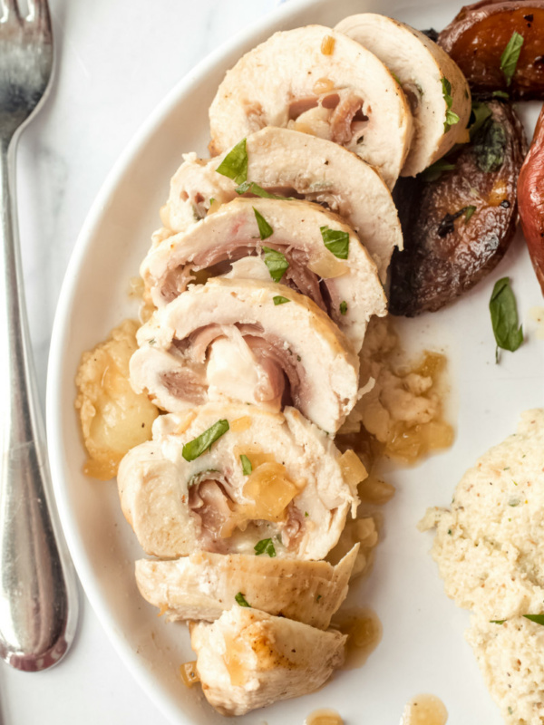 sliced chicken saltimbocca on a white plate with a fork on the side