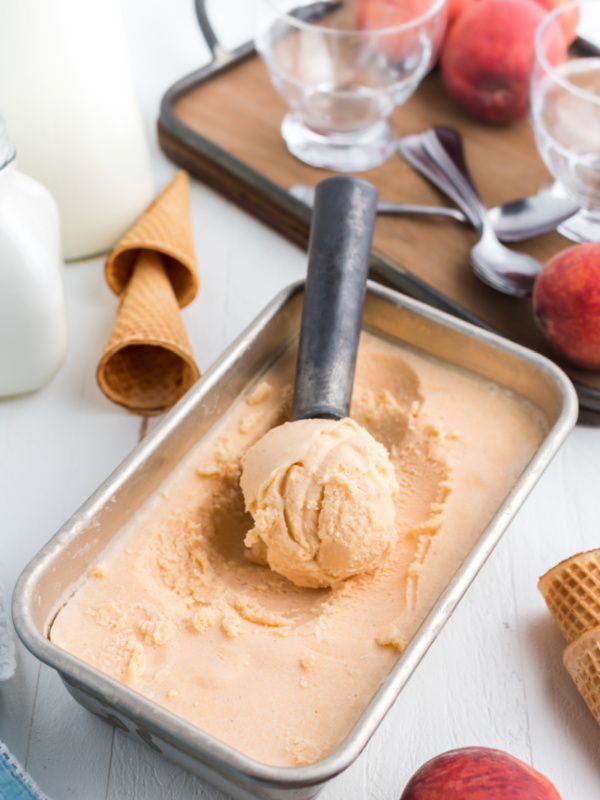 pan of fresh peach ice cream with scooper inside scooping a scoop