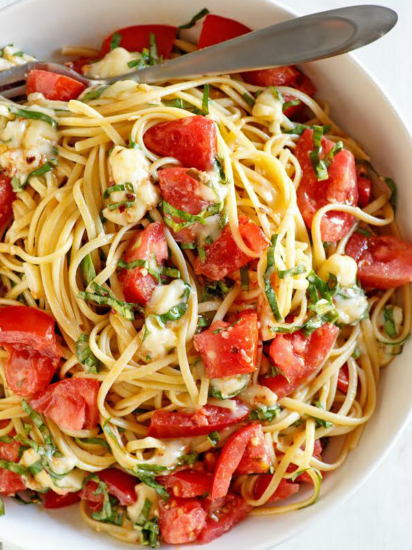 overhead shot of white bowl of linguine with tomatoes basil and brie with a fork