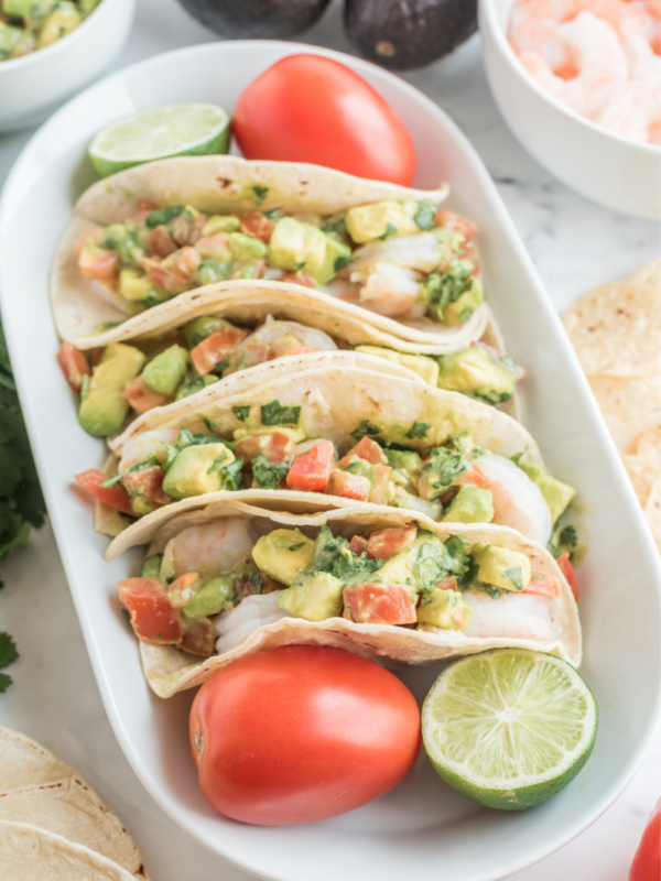 ceviche shrimp tacos displayed on a white platter with tomato and lime