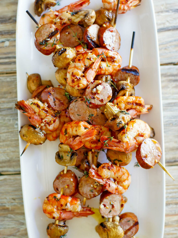 skewers of grilled shrimp sausage and mushrooms on a white platter