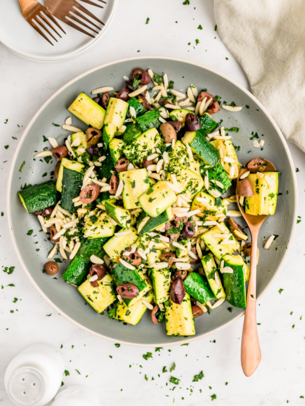 skillet with sauteed zucchini with almonds and olives and a spoon