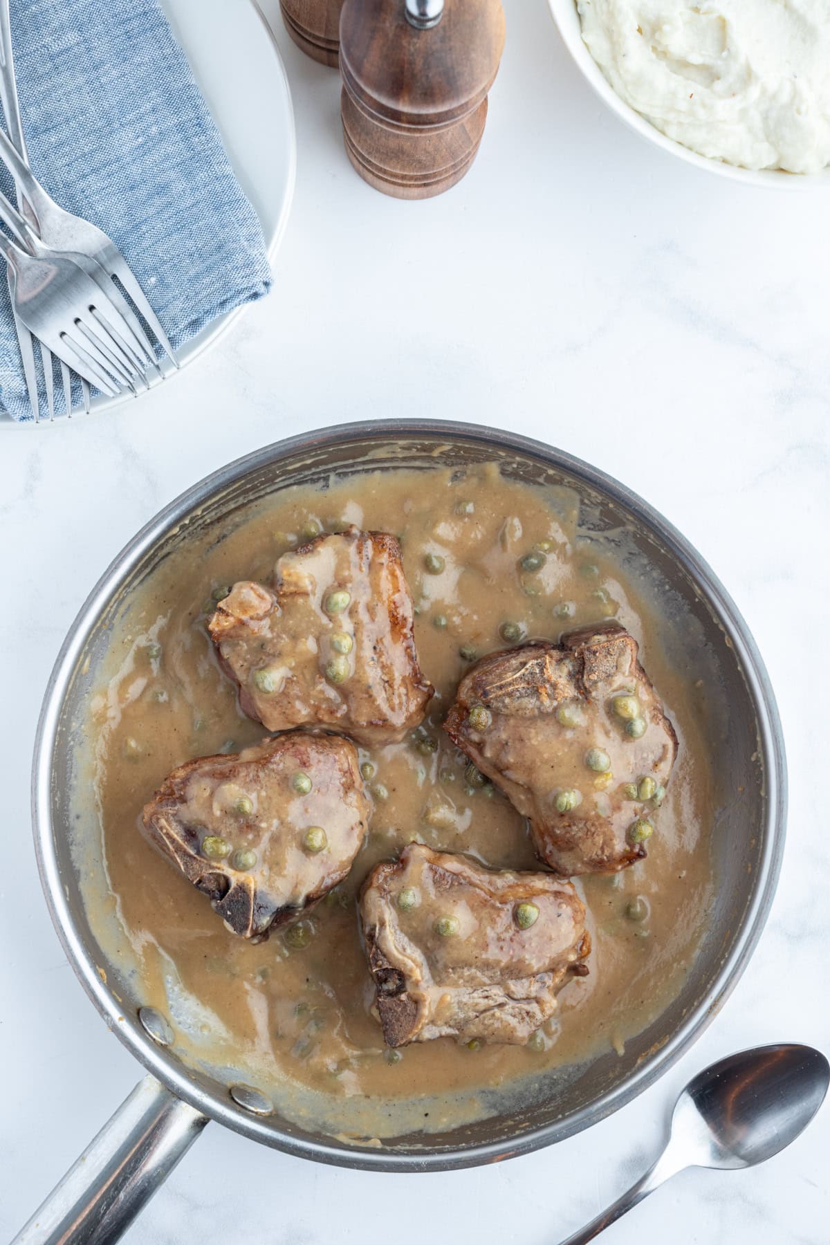 four lamb chops in pan with caper sauce on top