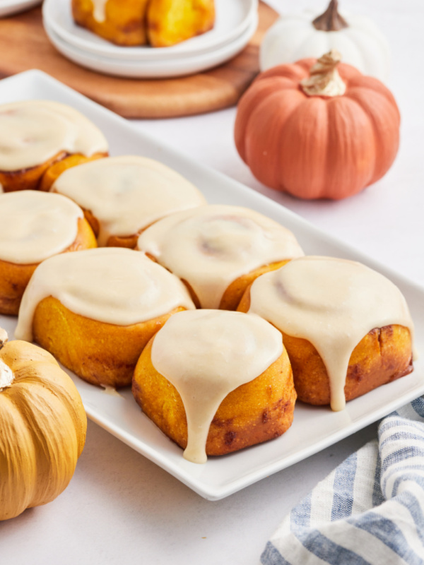 pumpkin cinnamon rolls with maple icing on a white platter