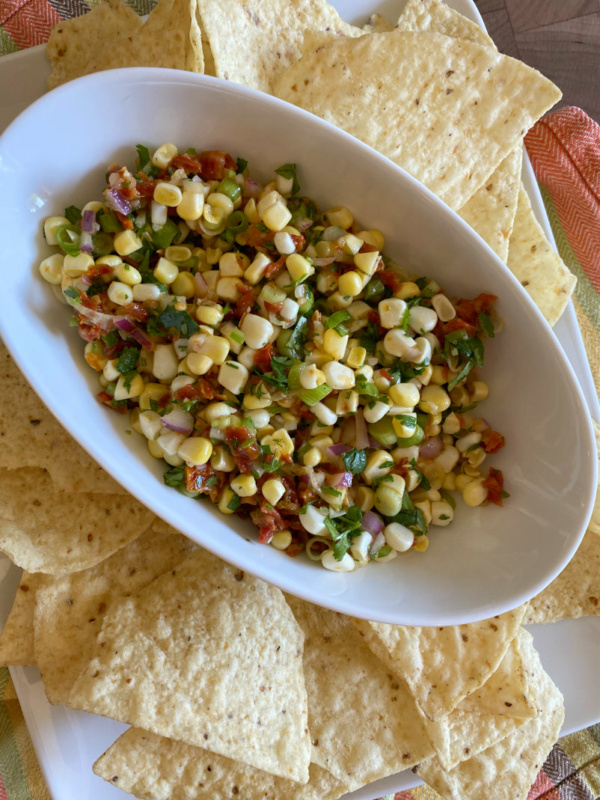 corn and sundried tomato salsa in a white bowl surrounded by tortilla chips