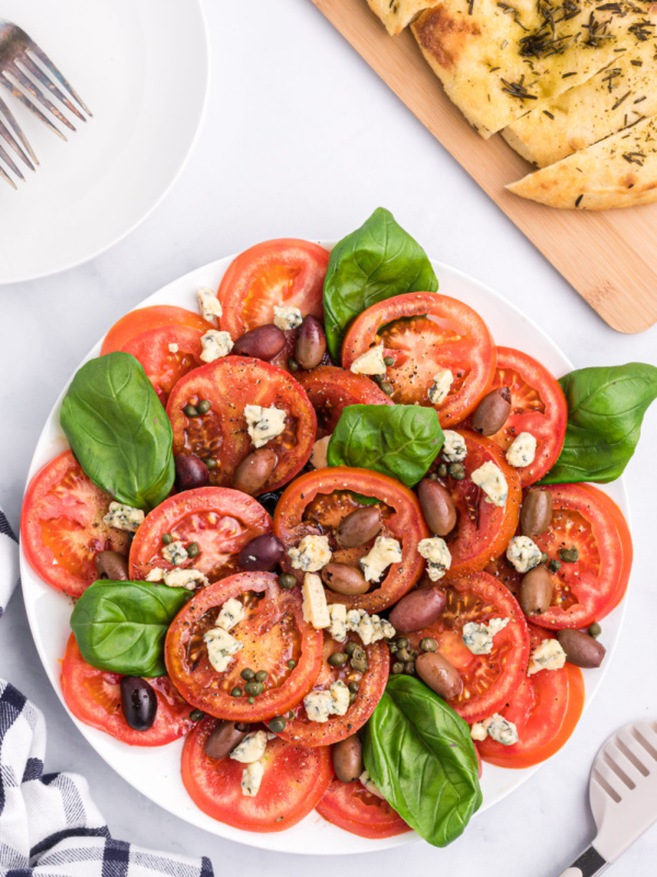 tomato caper and blue cheese salad on a white platter