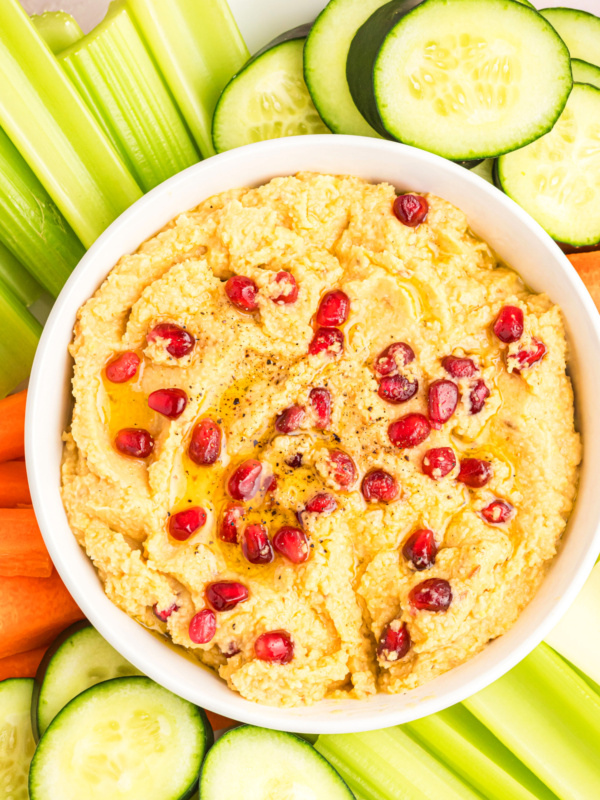 chickpea dip topped with pom seeds and veggies on side