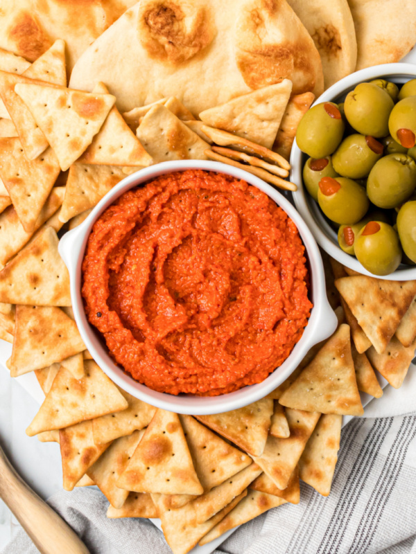 roasted red pepper almond spread in a white bowl with crackers and olives