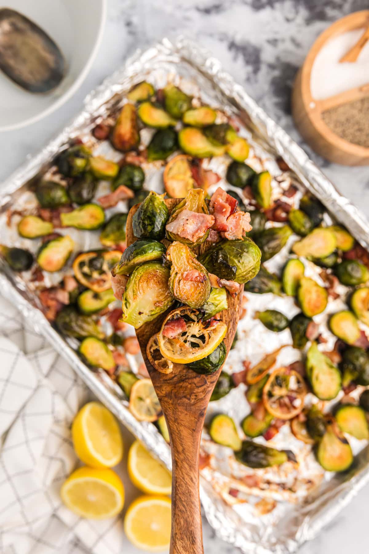 wooden spoon holding roasted brussels sprouts with lemon and bacon over baking sheet