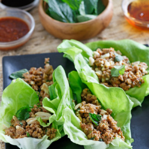 asian lettuce wraps on a black plate with bowls of ingredients in the background