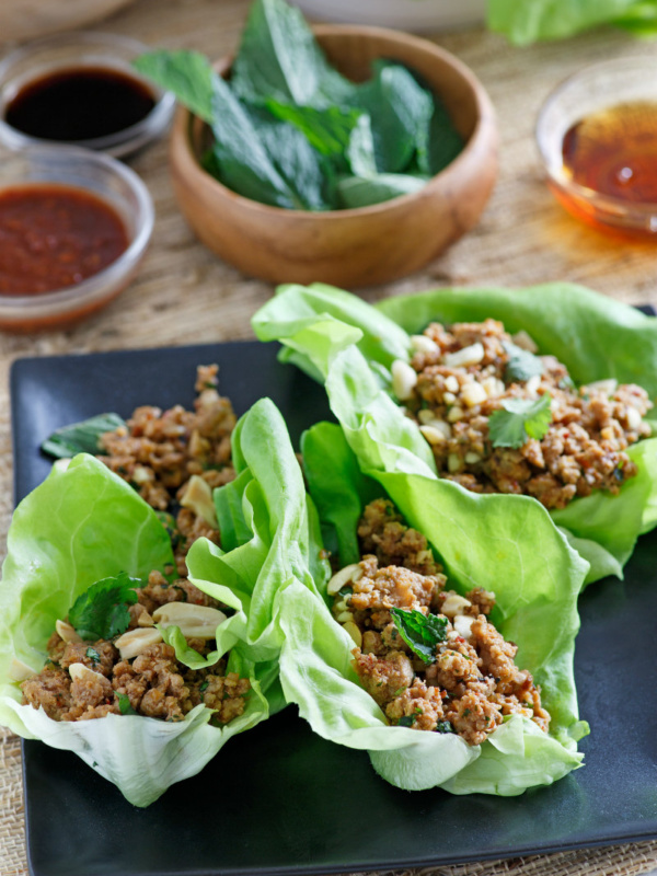 asian lettuce wraps on a black plate with bowls of ingredients in the background