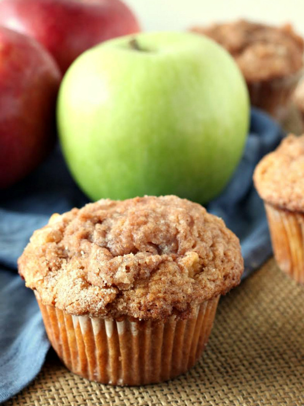 apple cinnamon muffin displayed in front of green and red apples with a blue cloth napkin