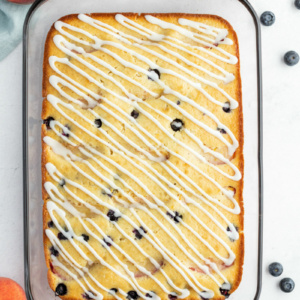 overhead shot of peach and blueberry coffee cake in a pyrex pan with fresh peaches and blueberries scattered in the background