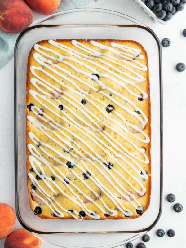 overhead shot of peach and blueberry coffee cake in a pyrex pan with fresh peaches and blueberries scattered in the background