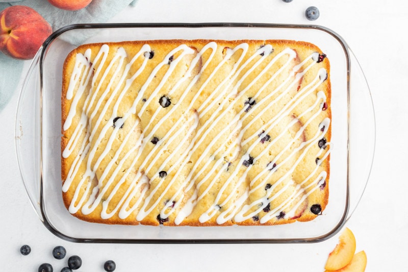 overhead shot of peach and blueberry coffee cake in a pyrex pan with fresh peaches and blueberries scattered in the background